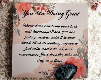 May include: A card with the text "You Are Doing Great" and a blue worry stone. The card has floral accents and text that reads, "Worry stone can bring good luck and harmony...Just breathe, take one day at a time."
