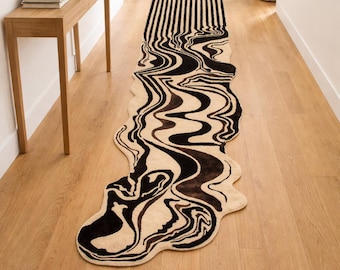 Pode incluir: Um tapete longo e abstrato com um design único. O tapete apresenta uma base creme com um padrão preto ondulado que cria um efeito líquido ou marmoreado. O tapete tem aproximadamente 244 cm de comprimento.