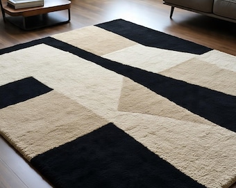Puede incluir: Alfombra con estampado geométrico en negro, beige y crema. La alfombra presenta un diseño moderno con formas y líneas angulares. La alfombra está hecha de un material suave y texturizado, adecuada para salones y dormitorios.