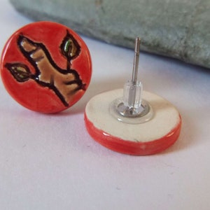 May include: A pair of red ceramic earrings with a brown and green twig design. The earrings have silver posts and backs.