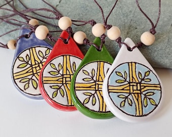 May include: Four ceramic pendant necklaces in blue, red, green, and white. Each pendant has a teardrop shape with a circular design featuring a yellow cross and green leaves. The pendants are strung on brown cords with wooden beads.
