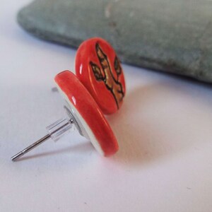 May include: A pair of red ceramic stud earrings with a brown dinosaur footprint design.