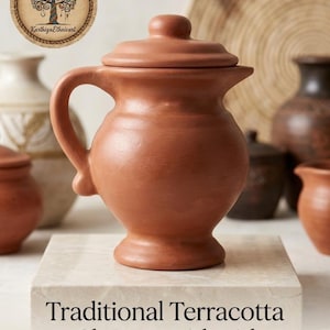Peut inclure: Une cruche en terre cuite avec un couvercle assorti, dotée d'un corps arrondi, d'une anse incurvée et d'une base évasée. Le texte "Traditional Terracotta Clay Jug with Lid" et "Préstine Craft" est imprimé sous la cruche sur une base claire.
