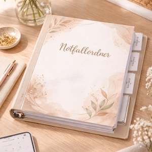 Könnte beinhalten: Ein beiger Ordner mit dem deutschen Text "Notfallordner" auf dem Cover, mit floralen und Blatt-Akzenten im Aquarellstil. Der Ordner hat beschriftete Register und liegt offen auf einer Holzoberfläche, mit Blumen und einem Stift in der Nähe.