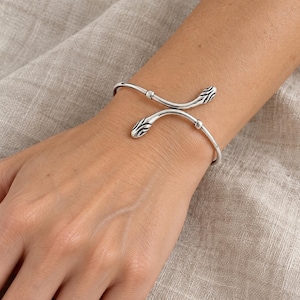Op de afbeelding: Een zilverkleurige metalen armband met een bypass-ontwerp en twee gestileerde slangenkop-uiteinden. Het metaal heeft een geoxideerde afwerking in de uitsparingen van de slangenkoppen, wat contrasteert met het gepolijste zilveren oppervlak.