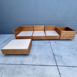 May include: A mid-century modern style wooden sofa and coffee table set. The sofa is composed of four modular sections with light-colored cushions. The coffee table is a low, square design. The furniture is made of light-colored wood.