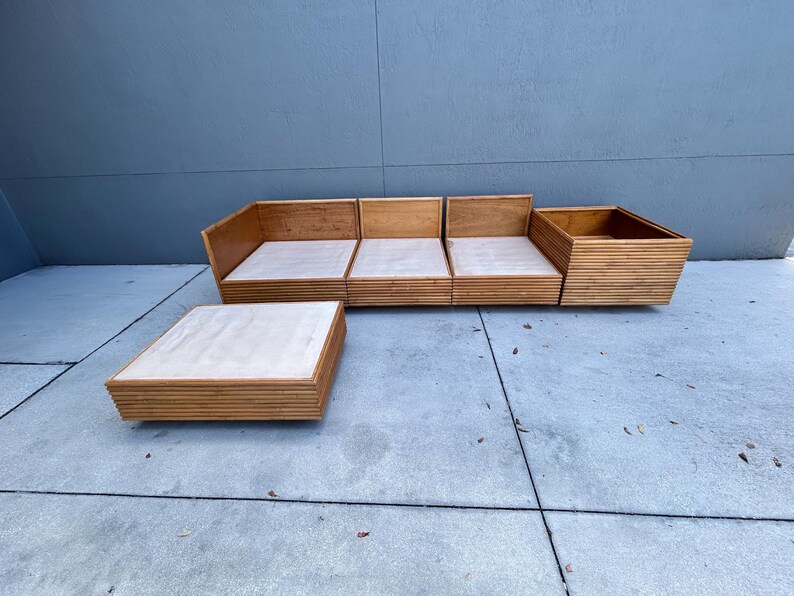 May include: A mid-century modern style wooden sofa and coffee table set. The sofa is composed of four modular sections with light-colored cushions. The coffee table is a low, square design. The furniture is made of light-colored wood.