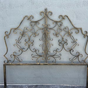 May include: A gold metal headboard with a decorative, ornate design featuring intricate swirls and scrolls. The headboard is made of wrought iron and has a classic, elegant style.