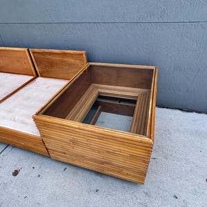 May include: A mid-century modern sofa and coffee table set. The sofa features a light-colored cushion and wooden frame. The coffee table has a glass top and a bamboo-style frame. The set is in good condition and appears to be well-maintained.