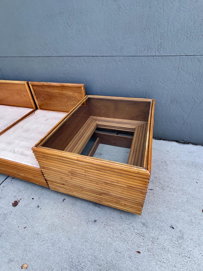 May include: A mid-century modern sofa and coffee table set. The sofa features a light-colored cushion and wooden frame. The coffee table has a glass top and a bamboo-style frame. The set is in good condition and appears to be well-maintained.