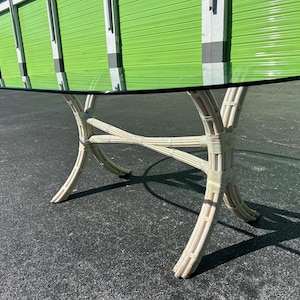 May include: White wicker oval dining table with a glass top. The table is in a warehouse setting with green garage doors in the background.