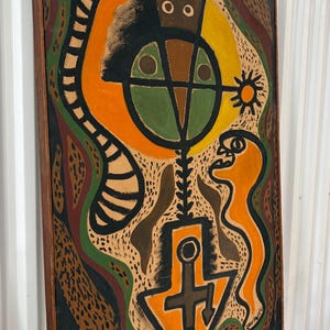 May include: A rectangular framed painting featuring abstract shapes and figures in black, orange, green, and brown. The composition includes a central circular form, a downward-pointing arrow shape, and a long striped tail-like element.
