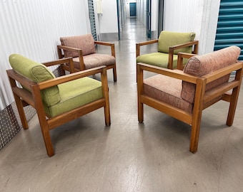 May include: Four mid-century modern armchairs with wooden frames. Two chairs have green cushions, and two have pink cushions. The chairs are arranged in a square formation, showcasing their design and style.