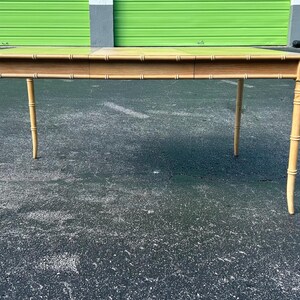 May include: A light-colored wooden table with a rectangular top and four slender, bamboo-style legs. The table is approximately 60 inches long and 30 inches wide, with a light-colored finish. The table is suitable for a living room or dining room.