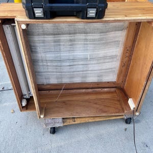 May include: A wooden cabinet with a mesh screen and a fluorescent light fixture inside. The cabinet is on wheels and has a black case on top. The dimensions are marked as 24" x 34".