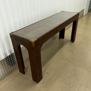 May include: A dark brown wooden console table with a glass top and brass accents. The table has a rectangular shape and four legs.