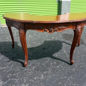 May include: A semi-circular wooden console table with a smooth, polished top and a curved apron. The piece features intricate floral and leaf carvings along the front edge and down the four cabriole legs, finished in a warm, medium-brown wood tone.