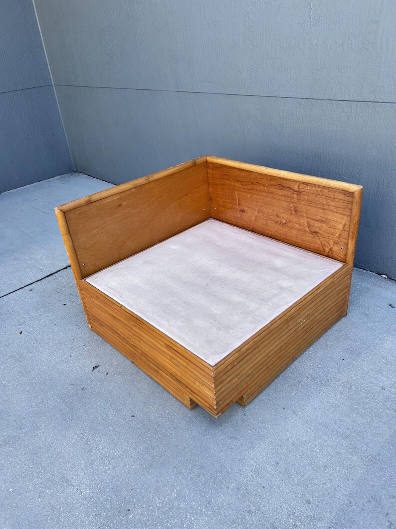 May include: A corner wooden chair with a light gray seat. The chair is made of light brown wood and has a simple, boxy design. The chair is approximately 30 inches wide and 30 inches deep.