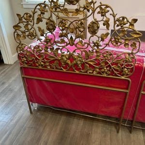 May include: A gold-colored metal bed frame with a floral design on the headboard. The bed frame has a red mattress and clear acrylic feet. The headboard features roses and other flowers.