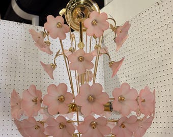 Könnte beinhalten: Ein Vintage-Kronleuchter mit floralem Design. Die Leuchte verfügt über rosa blütenförmige Schirme und goldfarbene Metallakzente. Der Kronleuchter ist an der Decke aufgehängt und für mehrere Glühbirnen ausgelegt.