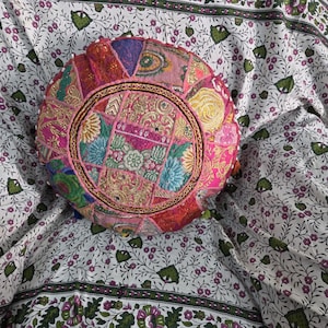 May include: A round, multi-colored patchwork floor cushion featuring intricate embroidery, metallic thread accents, and small circular mirrors. The cushion displays a vibrant mix of pink, gold, blue, and green fabric segments arranged in a circular pattern.