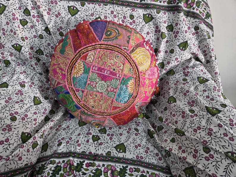 May include: A round, multi-colored patchwork floor cushion featuring intricate embroidery, metallic thread accents, and small circular mirrors. The cushion displays a vibrant mix of pink, gold, blue, and green fabric segments arranged in a circular pattern.