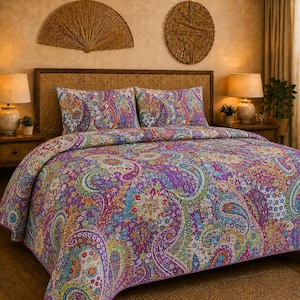 May include: A quilted bedspread and two matching pillow shams featuring a vibrant, multi-colored paisley pattern in shades of purple, orange, green, and blue. The bedding set is displayed on a bed with a woven cane headboard and neutral walls.