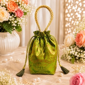 May include: A drawstring pouch crafted from vibrant green fabric with a subtle gold-toned woven pattern. The bag features a single twisted gold rope handle at the top and two matching green braided drawstrings finished with small green tassels.