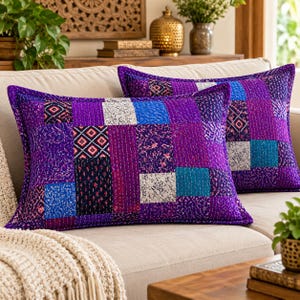 May include: Two rectangular throw cushions featuring a patchwork design of purple, blue, and white fabric squares. The cushions are decorated with intricate white kantha stitching throughout, creating a textured surface across the varied patterns.