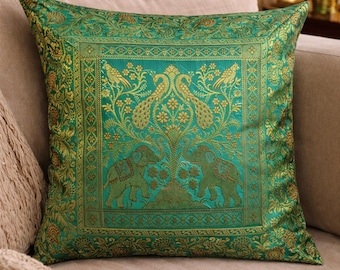 May include: A square throw pillow featuring a vibrant emerald green and gold woven fabric. The design displays a central panel with two elephants and two peacocks surrounded by floral motifs, framed by a decorative border of repeating patterns.