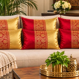 Peut inclure: Un ensemble de six coussins rectangulaires présentant un coloris rouge et doré éclatant. Chaque coussin est divisé en trois sections verticales, avec une bande centrale de motifs floraux rouges et dorés entourée de panneaux unis rouge et or.