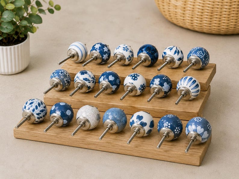 Pu&ograve; includere: Una collezione di diciotto pomelli rotondi in ceramica per mobili con vari motivi blu e bianchi, inclusi disegni floreali, a righe, a cuore e a stella. Ogni pomello ha un perno in metallo color argento ed &egrave; disposto su un espositore in legno a tre livelli.