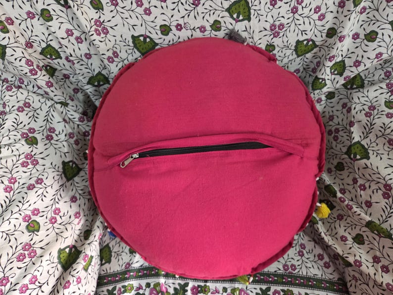 May include: A round, solid hot pink cushion featuring a black zipper closure running horizontally across the center of the back panel. The fabric appears to be a plain weave textile, and the circular shape is consistent throughout the design.