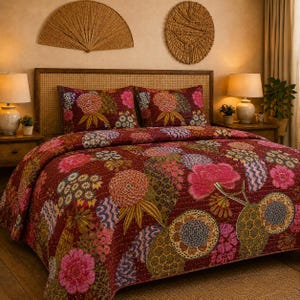 May include: A deep red quilt and two matching pillow shams featuring a repeating pattern of large, stylised floral motifs in shades of pink, orange, yellow, and blue, with visible kantha-style stitching throughout the fabric surface.