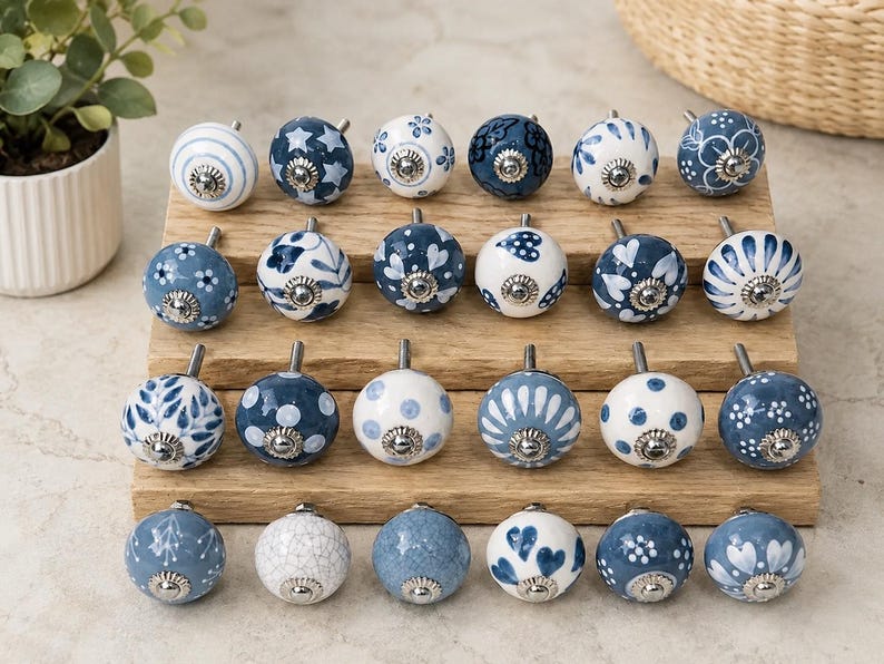 Pu&ograve; includere: Una collezione di ventiquattro pomelli rotondi in ceramica per mobili con vari motivi blu e bianchi, tra cui strisce, stelle, pois, motivi floreali e cuori. Ogni pomello ha una base in metallo color argento e una vite centrale.