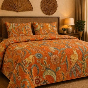 May include: A quilted bedspread and two matching pillow shams featuring a vibrant orange base color with a multi-colored floral and bird pattern in shades of blue, green, and yellow. The bedding set has a stitched texture throughout the fabric.