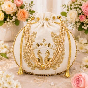 Peut inclure: Une pochette à cordon de couleur crème ornée de broderies dorées représentant deux paons face à face. Le sac est décoré de multiples rangs de fausses perles blanches et de perles dorées, avec des cordons métalliques et des pompons dorés.