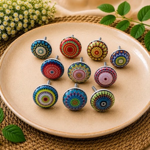 May include: A collection of ten round cabinet knobs featuring diverse, vibrant, and intricate circular mandala-style patterns in various colour combinations including red, blue, green, yellow, and pink, each with a central metal screw attachment.
