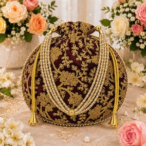 Könnte beinhalten: Ein tiefburgunderroter Samtbeutel mit Kordelzug, der mit aufwendigen Goldfadenstickereien in einem Blumenmuster verziert ist. Die Tasche verfügt über einen mehrsträngigen Perlenhenkel und goldfarbene Metallakzente an den Kordelenden.