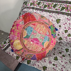 May include: A round, multi-colored patchwork floor cushion featuring intricate embroidery, small circular mirrors, and vibrant fabric panels in shades of pink, orange, yellow, and blue, finished with small decorative tassels along the outer edge.