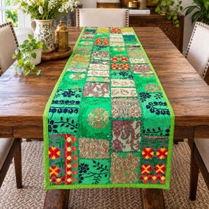 Può includere: Un runner da tavola rettangolare caratterizzato da un vivace design patchwork verde composto da vari quadrati di tessuto. Il runner presenta un mix di motivi floreali, paisley e geometrici nei toni del rosso, oro, bianco e nero, con un bordo verde.
