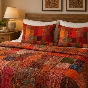Peut inclure: Un couvre-lit en patchwork et deux taies d'oreiller assorties présentant une gamme vibrante de panneaux de tissu carrés dans des tons de rouge, orange, jaune et brun profond. L'ensemble textile affiche divers motifs floraux et géométriques.