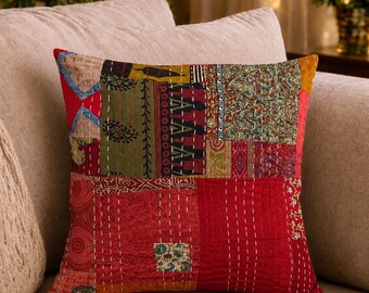 Op de afbeelding: Een vierkant sierkussen met een patchworkontwerp van diverse stoffen in tinten rood, olijfgroen en bruin. Het oppervlak is versierd met gedetailleerd wit kantha-stiksel, wat zorgt voor een getextureerd en doorgestikt uiterlijk van het kussen.