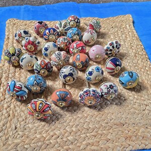 May include: A collection of round ceramic cabinet knobs featuring various hand-painted floral and geometric patterns in vibrant colours including red, blue, yellow, pink, and green, each finished with a central gold-toned metal hardware fitting.