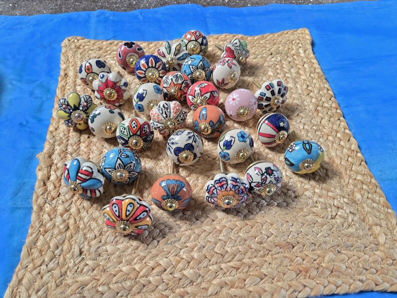 May include: A collection of round ceramic cabinet knobs featuring various hand-painted floral and geometric patterns in vibrant colours including red, blue, yellow, pink, and green, each finished with a central gold-toned metal hardware fitting.