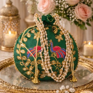 Peut inclure: Une pochette ronde verte à cordon de serrage ornée de broderies florales métalliques dorées et de deux paons brodés aux ailes roses et bleues. Le sac est agrémenté de longues anses en perles blanches et de pompons en métal doré.