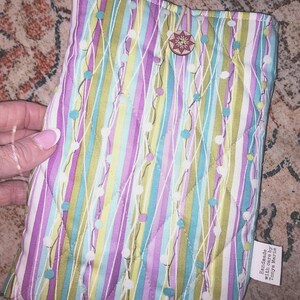 Könnte beinhalten: Gesteppte Stoffhülle mit einem farbenfrohen Streifenmuster in Lila, Grün und Blau. Die Hülle hat einen dekorativen Knopfverschluss und ein Etikett mit der Aufschrift "Handmade with care by Tonya Marie."