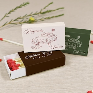 May include: Three rectangular matchboxes featuring a line drawing of a convertible car with the text Just Married, Benjamin, Amelia, Malibu, CA, and July 21, 2027. The boxes are white, dark green, and dark brown, containing matches with red tips.