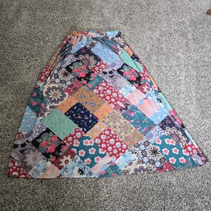 May include: A patchwork maxi skirt featuring a variety of floral and geometric patterns in shades of red, blue, green, and orange. The skirt has an elastic waistband and a flowing silhouette, perfect for a bohemian style.
