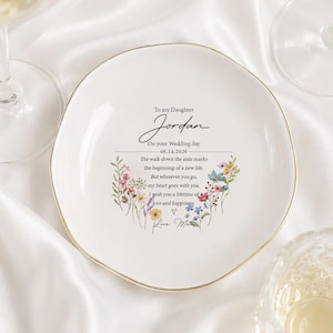 May include: A white ceramic trinket dish with an irregular, organic shape and a gold-painted rim. The center features black text reading To my Daughter Jordan On your Wedding day 06.14.2026, surrounded by a colorful floral illustration and a message.